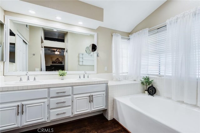 bathroom featuring double vanity, a garden tub, vaulted ceiling, and a sink