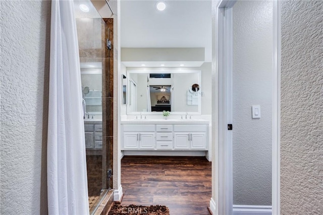 full bathroom featuring a textured wall, a stall shower, a sink, and wood finished floors