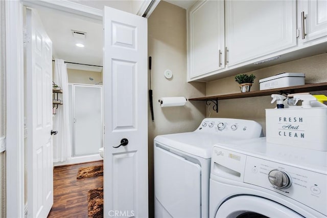 clothes washing area featuring visible vents, dark wood-style flooring, washing machine and dryer, and cabinet space