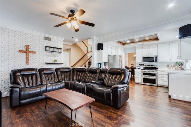 living room featuring dark wood-style flooring, visible vents, ornamental molding, stairway, and wallpapered walls