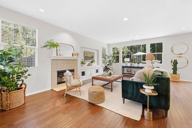 living area with a wealth of natural light, baseboards, a tiled fireplace, and wood finished floors