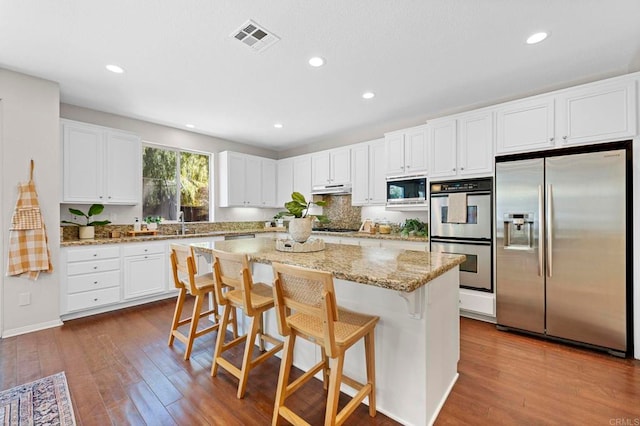 kitchen with black appliances, a breakfast bar, visible vents, and white cabinets