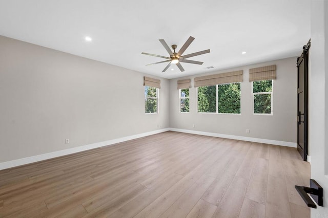 unfurnished room featuring a barn door, light wood-style flooring, a ceiling fan, and baseboards