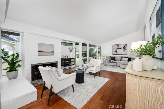 living room featuring a healthy amount of sunlight, dark hardwood / wood-style floors, vaulted ceiling, and a brick fireplace