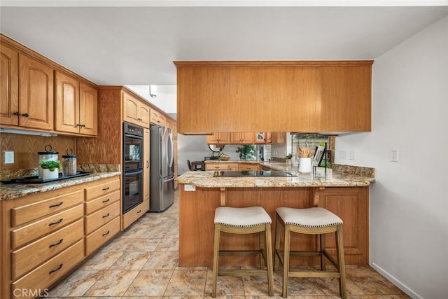 kitchen featuring stainless steel refrigerator, kitchen peninsula, double oven, and light stone counters