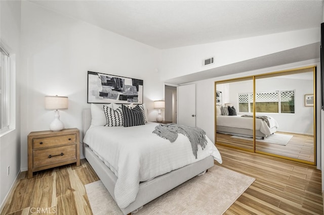 bedroom with a closet, vaulted ceiling, light hardwood / wood-style flooring, and a textured ceiling