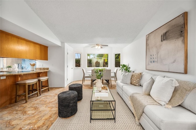 living room with ceiling fan, vaulted ceiling, and a textured ceiling