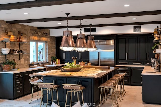 kitchen featuring a breakfast bar area, a center island, hanging light fixtures, built in fridge, and light stone countertops