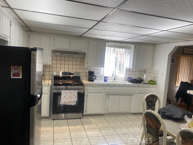 kitchen with sink, light tile patterned floors, appliances with stainless steel finishes, white cabinets, and tile countertops