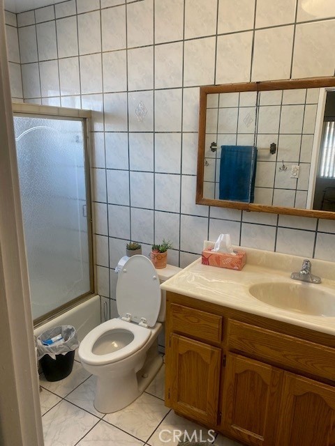 full bathroom featuring toilet, tile walls, vanity, enclosed tub / shower combo, and decorative backsplash