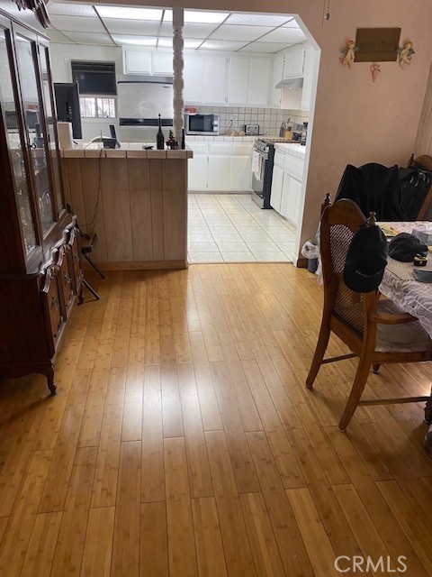 kitchen featuring backsplash, white cabinets, kitchen peninsula, stainless steel appliances, and light wood-type flooring