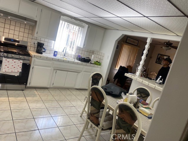 kitchen with white cabinetry, sink, tile counters, and stainless steel gas range