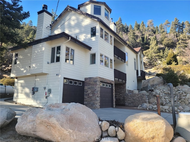 view of side of property featuring a garage, stone siding, driveway, and a chimney