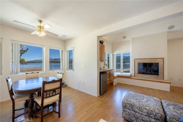 dining room with a glass covered fireplace, ceiling fan, baseboards, and light wood-type flooring