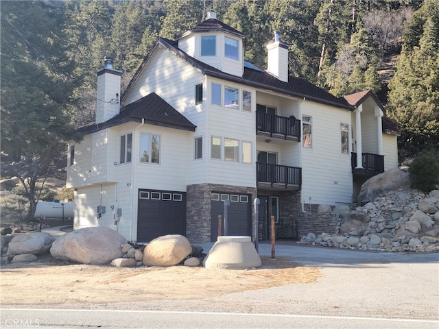 view of front facade with stone siding, a chimney, an attached garage, and a balcony