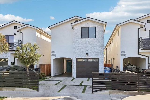 view of front facade featuring driveway, stone siding, an attached garage, fence, and stucco siding