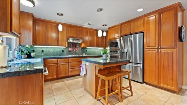 kitchen featuring sink, appliances with stainless steel finishes, hanging light fixtures, a center island, and a kitchen bar