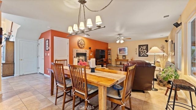 tiled dining area featuring ceiling fan with notable chandelier and a tile fireplace