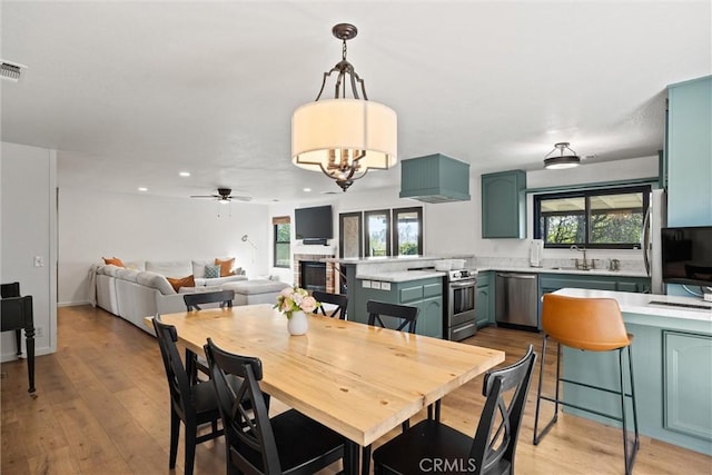 dining room featuring ceiling fan with notable chandelier, sink, and light wood-type flooring