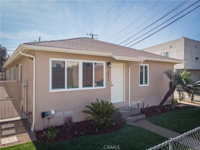 bungalow featuring entry steps, roof with shingles, fence, and stucco siding