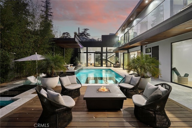 pool at dusk with a wooden deck and an outdoor fire pit