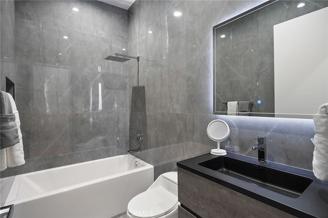 full bathroom featuring tiled shower / bath, tile walls, vanity, and toilet