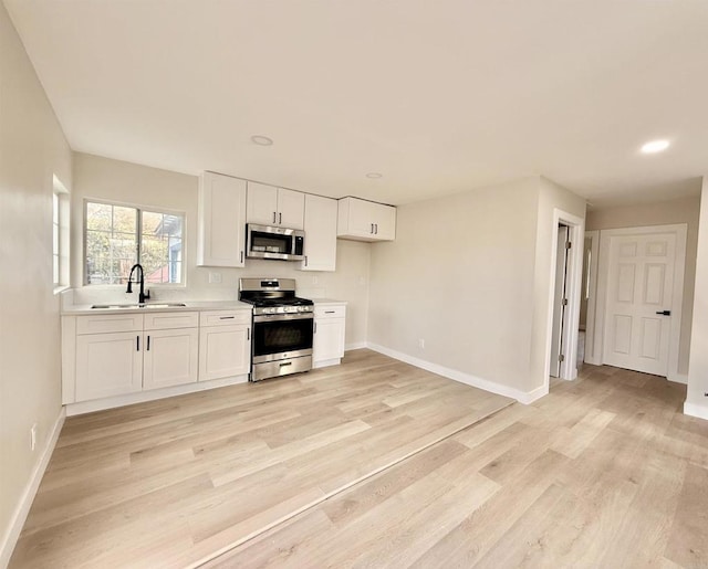 kitchen featuring light wood-style flooring, appliances with stainless steel finishes, light countertops, white cabinetry, and a sink