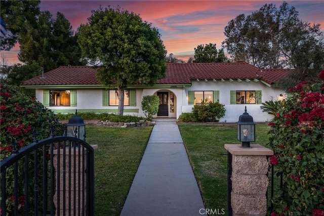 mediterranean / spanish home featuring a tiled roof, a lawn, and stucco siding