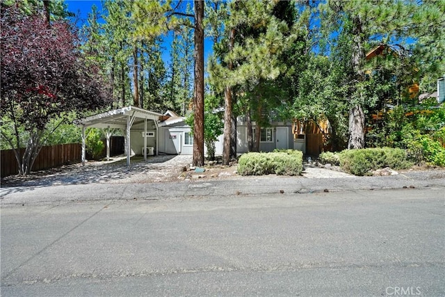 view of property hidden behind natural elements featuring driveway, fence, and a detached carport