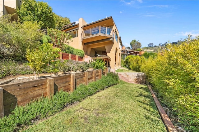 rear view of property featuring a lawn, fence, a balcony, and stucco siding