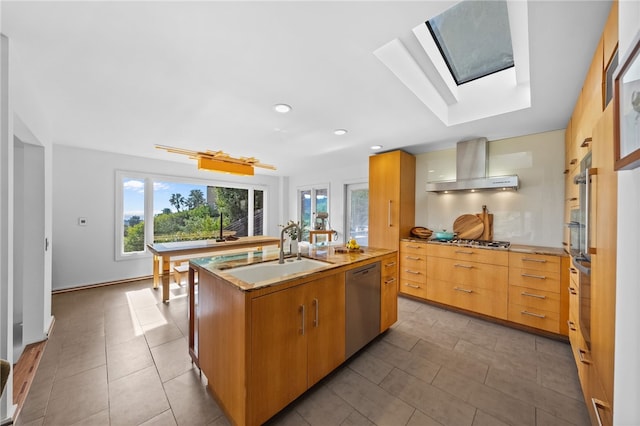 kitchen with an island with sink, stainless steel appliances, light countertops, wall chimney range hood, and a sink