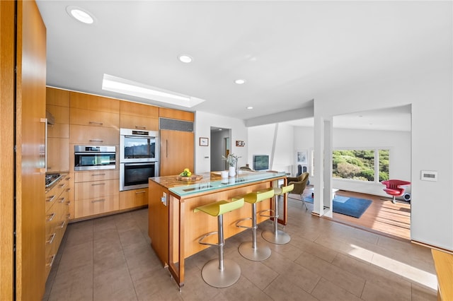 kitchen featuring double oven, a breakfast bar area, light countertops, modern cabinets, and a center island with sink