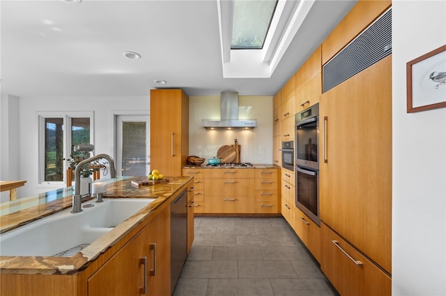 kitchen with a skylight, wall chimney exhaust hood, modern cabinets, stainless steel appliances, and a sink