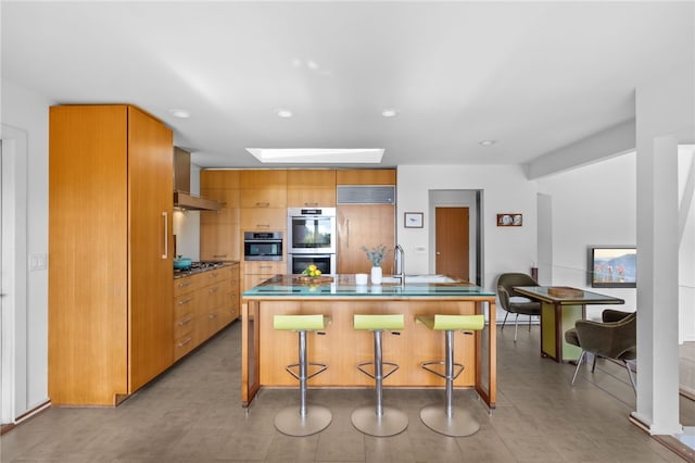 kitchen with a breakfast bar, a skylight, stainless steel appliances, an island with sink, and modern cabinets