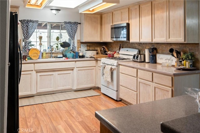 kitchen featuring light brown cabinetry, tasteful backsplash, black refrigerator, white gas range, and light hardwood / wood-style floors