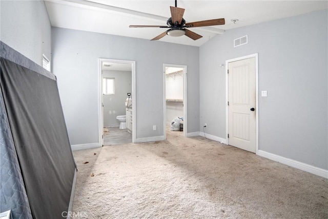 unfurnished bedroom with lofted ceiling, ceiling fan, ensuite bathroom, light carpet, and a walk in closet