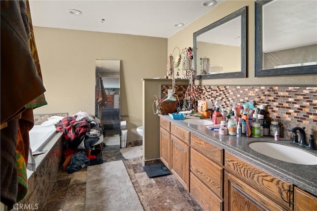 bathroom with tiled tub, vanity, toilet, and decorative backsplash