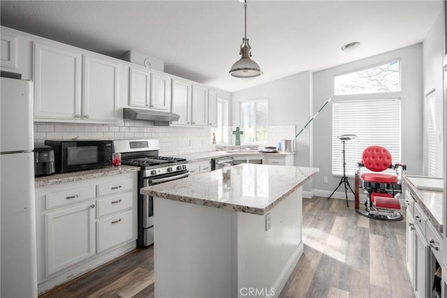 kitchen with appliances with stainless steel finishes, decorative light fixtures, white cabinets, a center island, and light stone counters