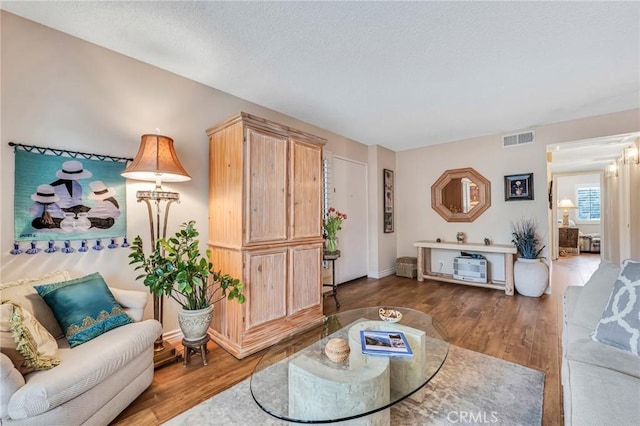 living area with baseboards, a textured ceiling, visible vents, and wood finished floors