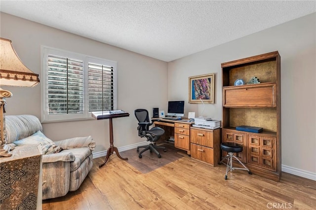 office with light wood-style flooring, baseboards, and a textured ceiling
