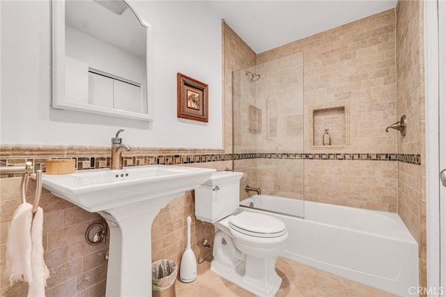 bathroom featuring tile patterned flooring, tile walls, toilet, a wainscoted wall, and washtub / shower combination
