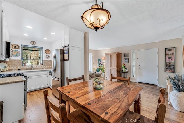 dining space featuring a chandelier, a textured ceiling, baseboards, light wood-style floors, and recessed lighting
