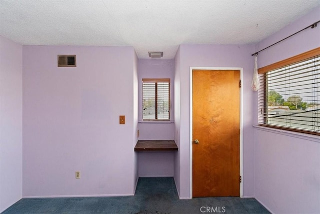 unfurnished bedroom with a textured ceiling and dark colored carpet