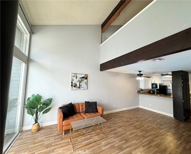 sitting room with ceiling fan, a textured ceiling, a towering ceiling, and hardwood / wood-style floors