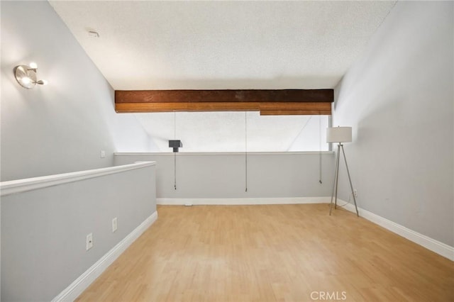 spare room featuring beam ceiling, wood-type flooring, and a textured ceiling