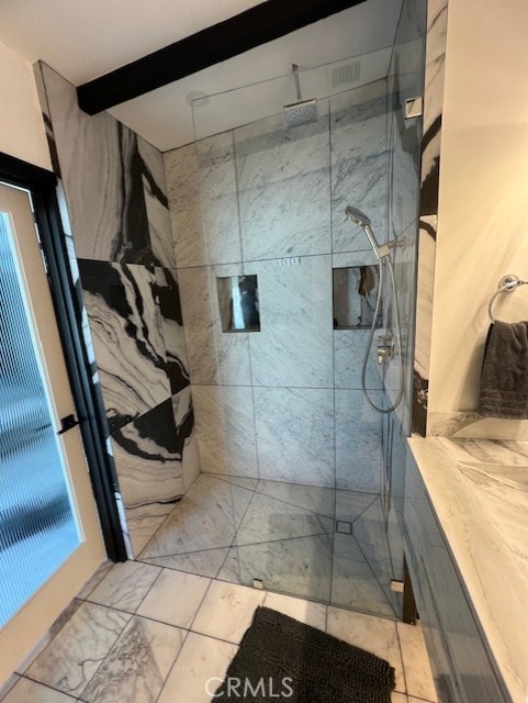 bathroom featuring a tile shower and beam ceiling