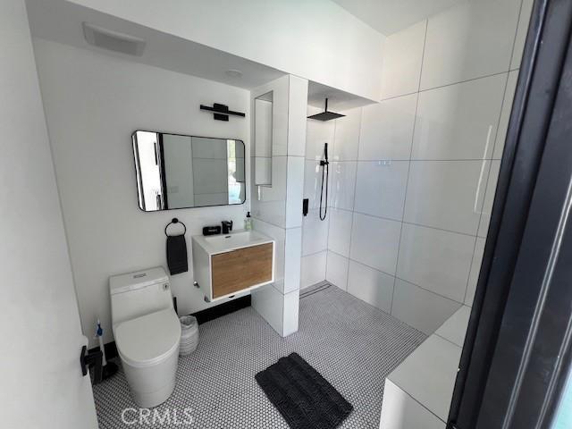 bathroom featuring tile patterned flooring, vanity, tiled shower, and toilet