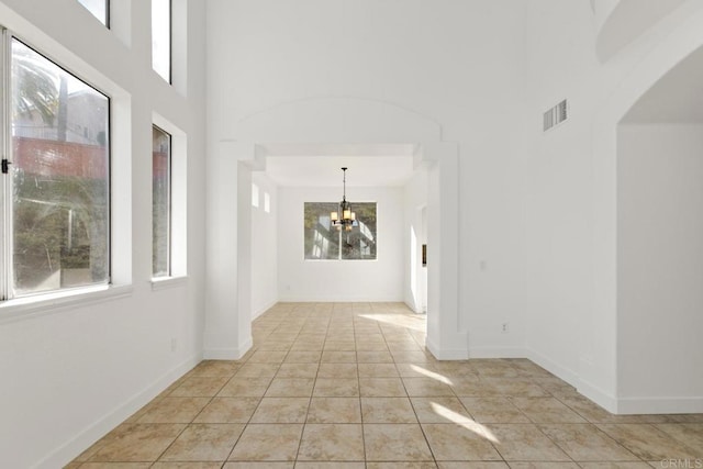 unfurnished room with arched walkways, an inviting chandelier, visible vents, and a wealth of natural light