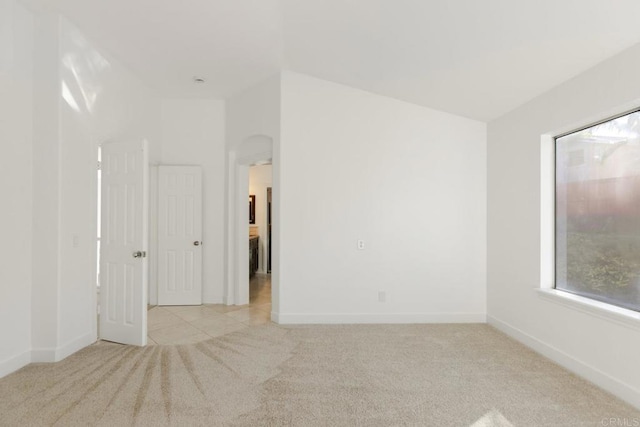 carpeted spare room featuring arched walkways and baseboards