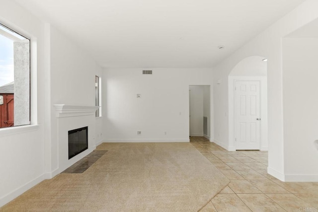 unfurnished living room with a fireplace with flush hearth, visible vents, baseboards, and light tile patterned floors